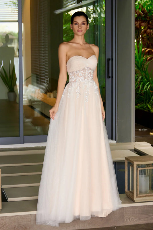 Woman wearing a strapless nude wedding gown with floral details in an outdoor setting.