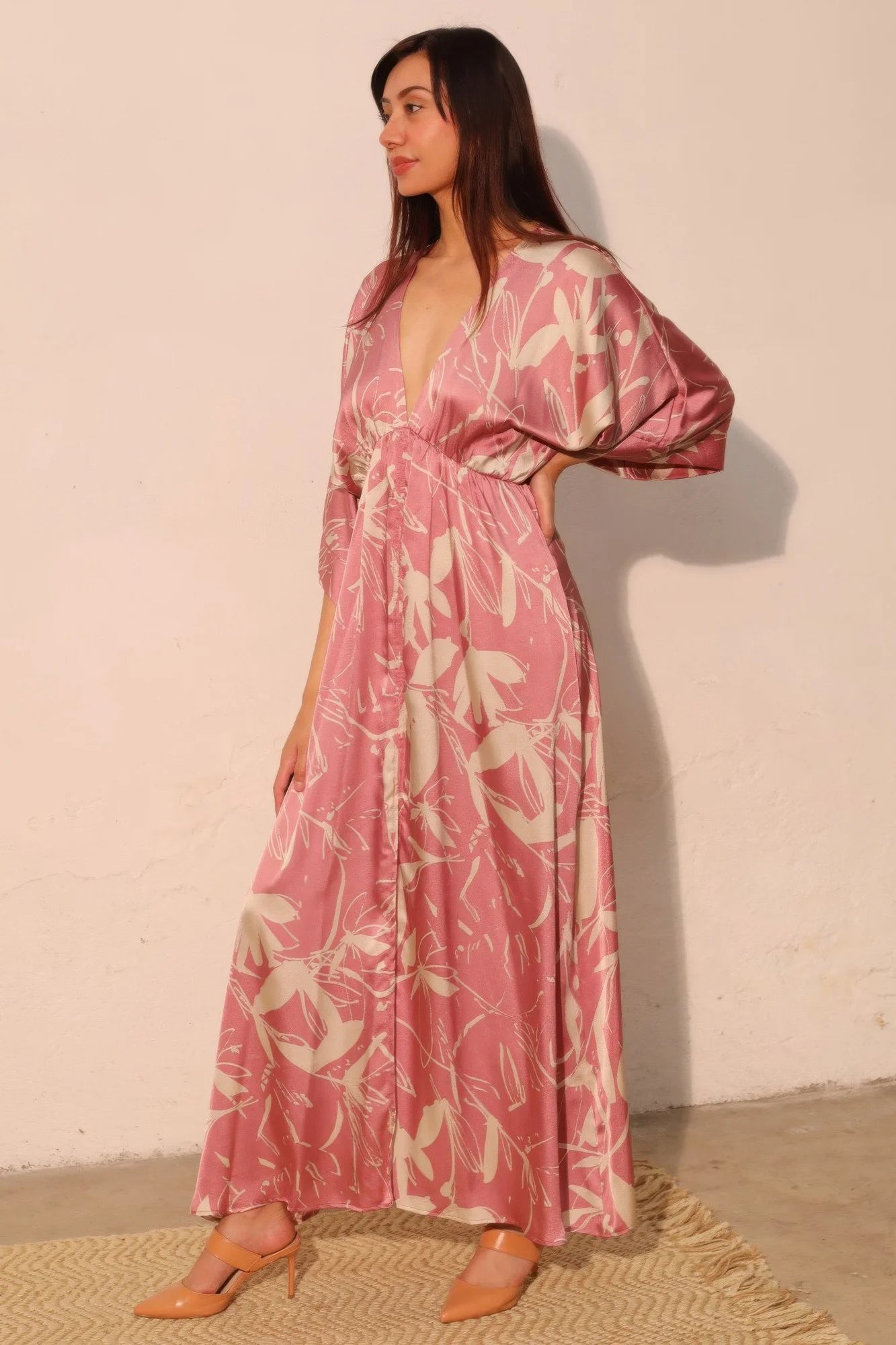Woman wearing a pink floral dress against a plain wall.