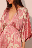 Woman wearing a pink floral kimono-style garment against a plain background