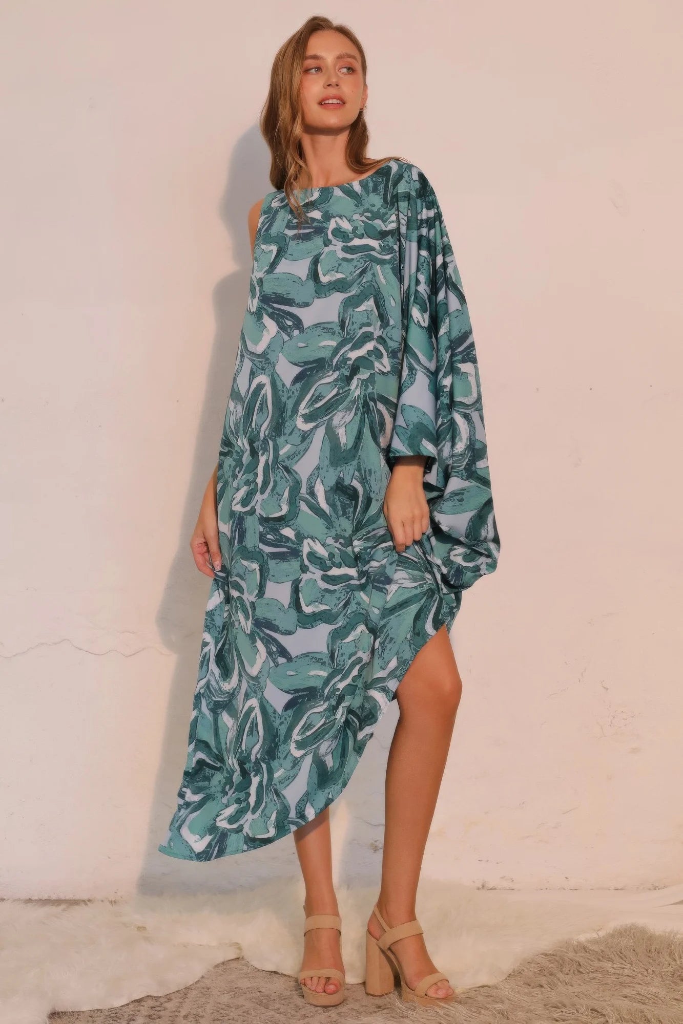 Woman wearing a green leaf-patterned dress against a white wall