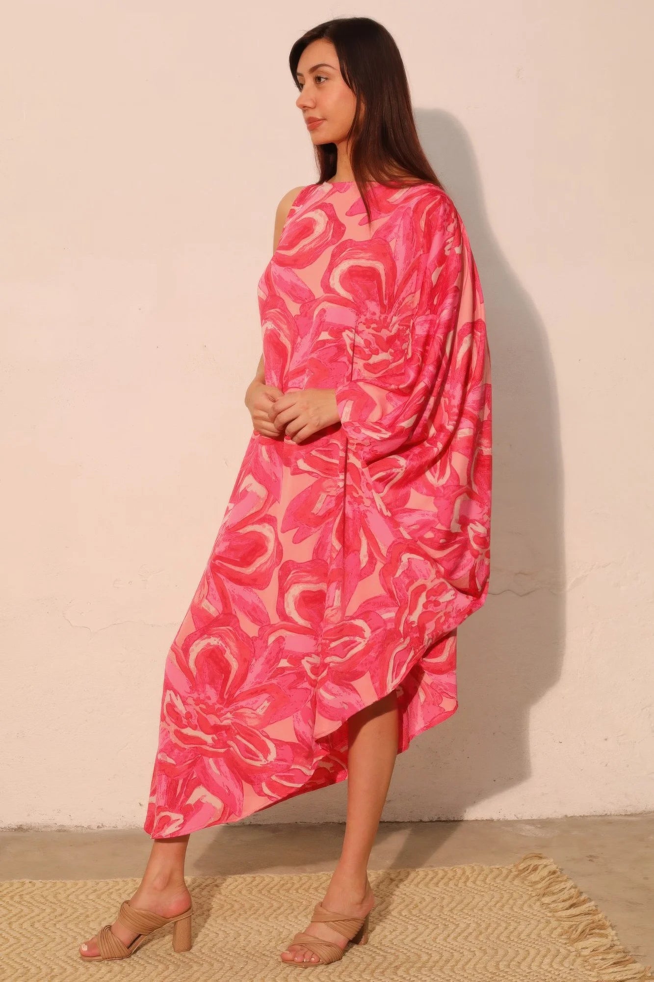 Woman wearing a pink patterned dress against a beige wall.
