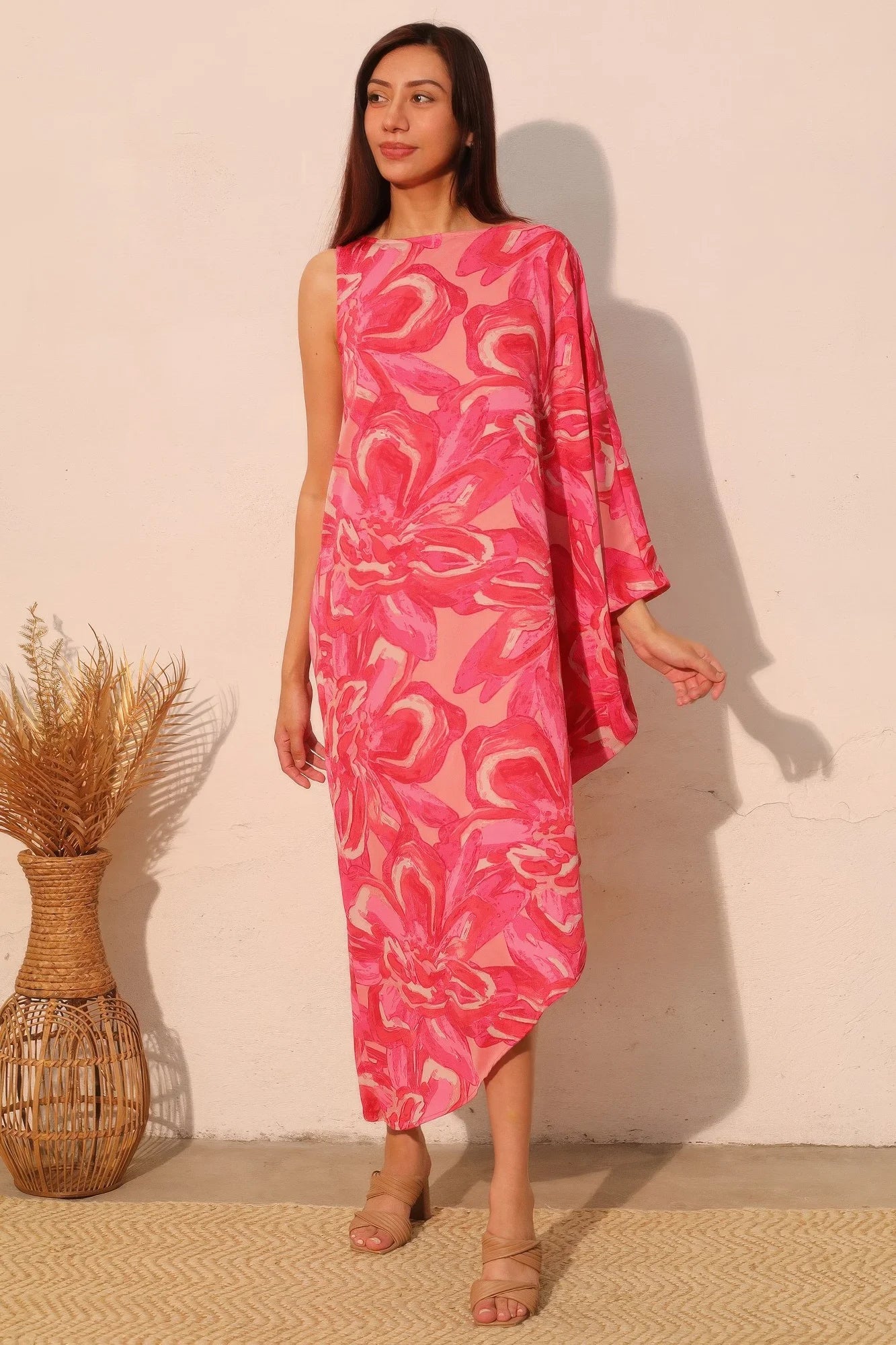 Woman wearing a pink patterned dress standing against a plain wall with a woven basket.
