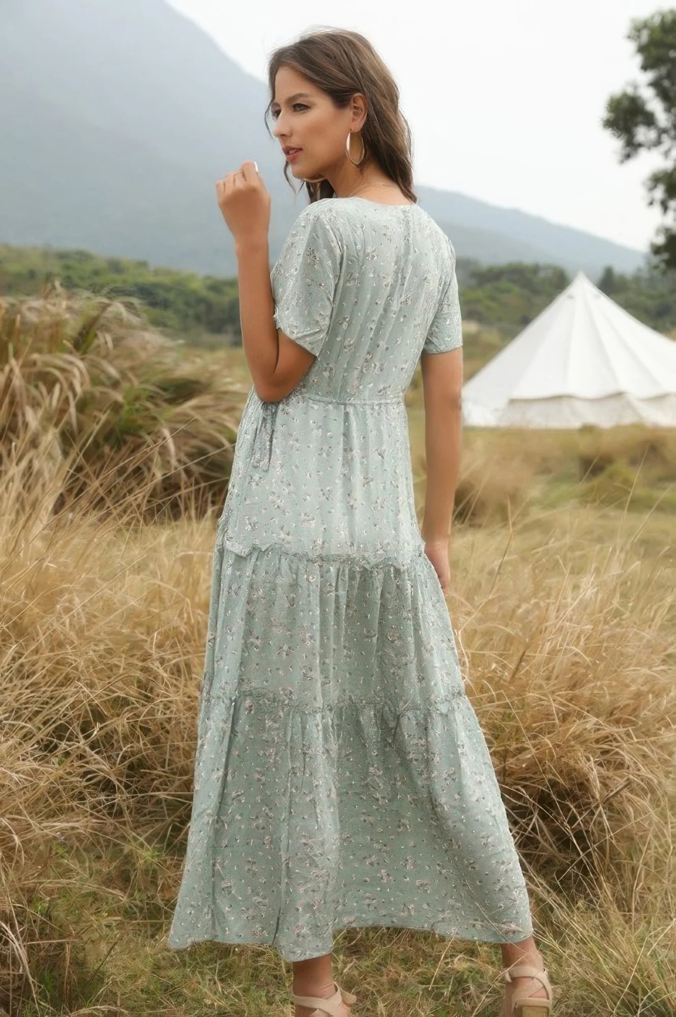 Woman in a light green dress standing in a field with mountains in the background