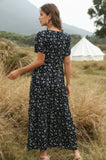 Woman in a black floral dress standing in a field with a tent in the background
