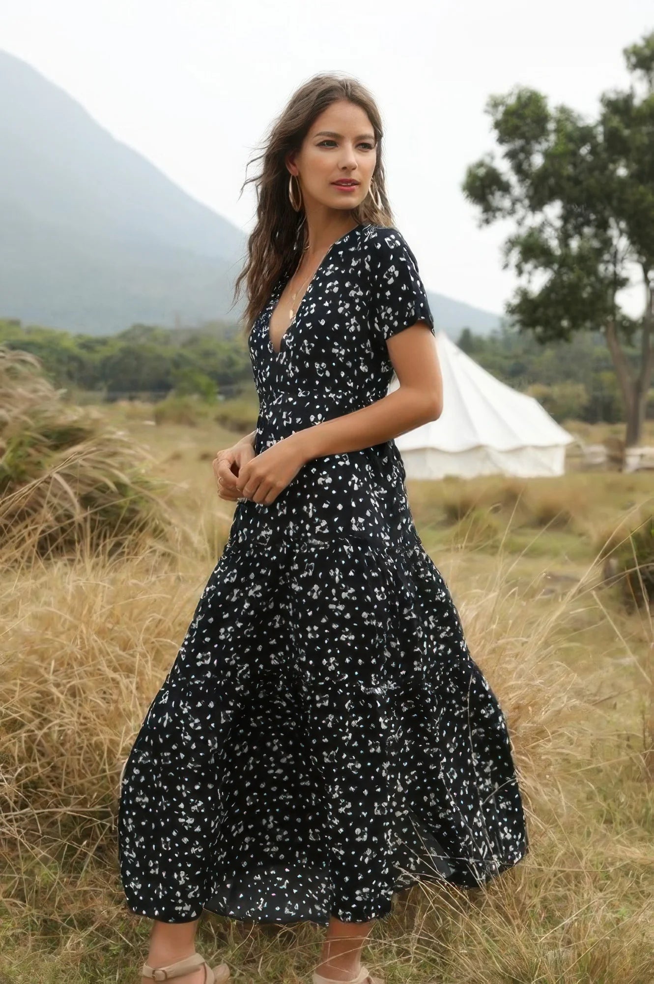 Woman in a black floral dress standing in a field with mountains in the background