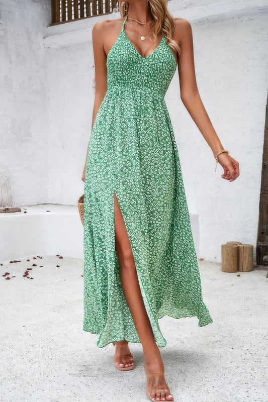 Woman wearing a green floral dress with a slit, standing against a white wall.