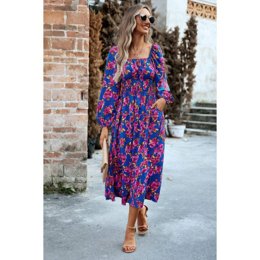 Woman wearing a blue floral dress standing against a brick wall.