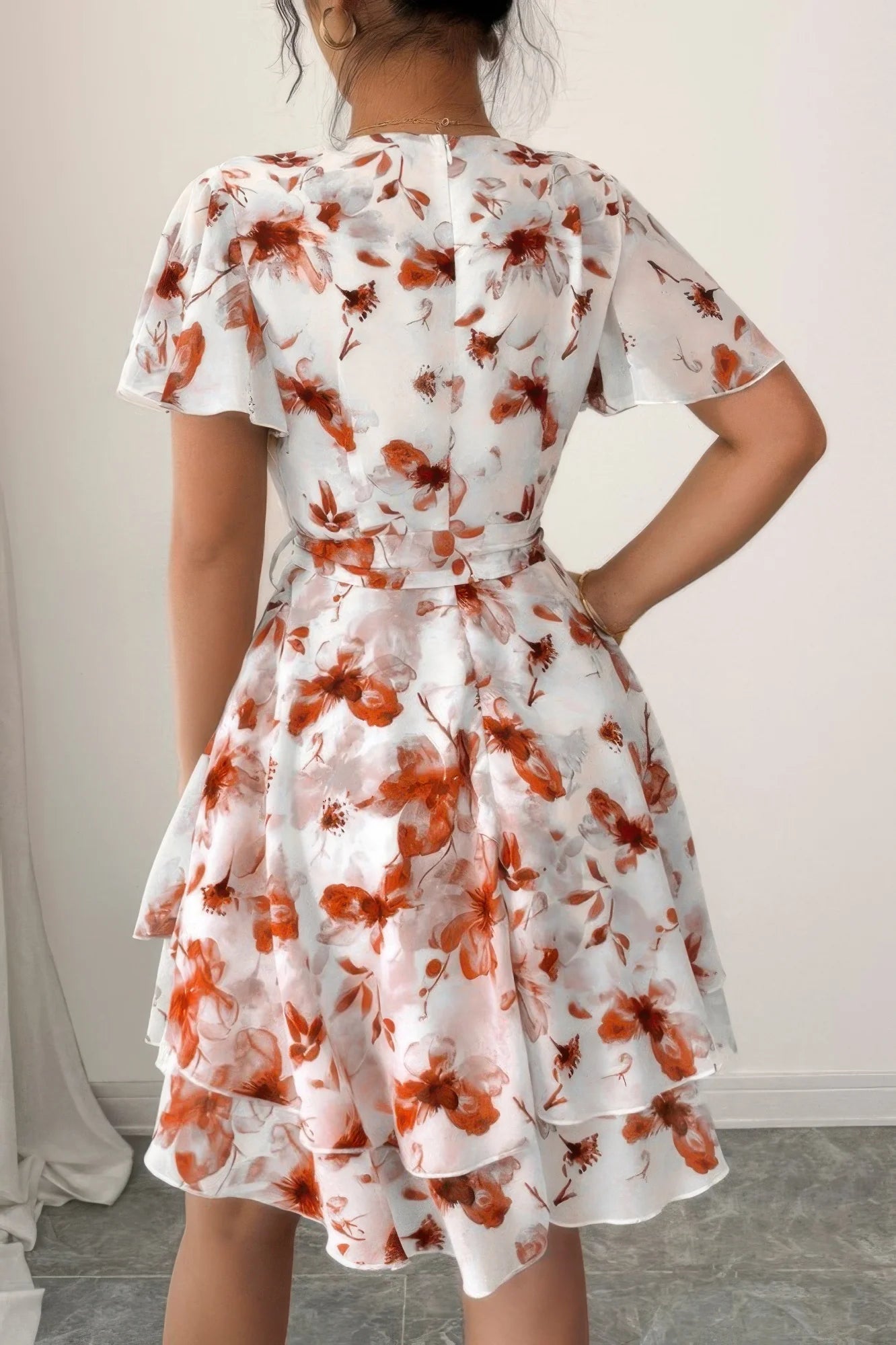 Woman wearing a white dress with red floral pattern against a plain background