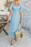 Woman in a light blue dress holding a straw bag in an outdoor setting.