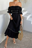 Woman wearing a black off-shoulder dress with a straw bag, standing on a stone floor.
