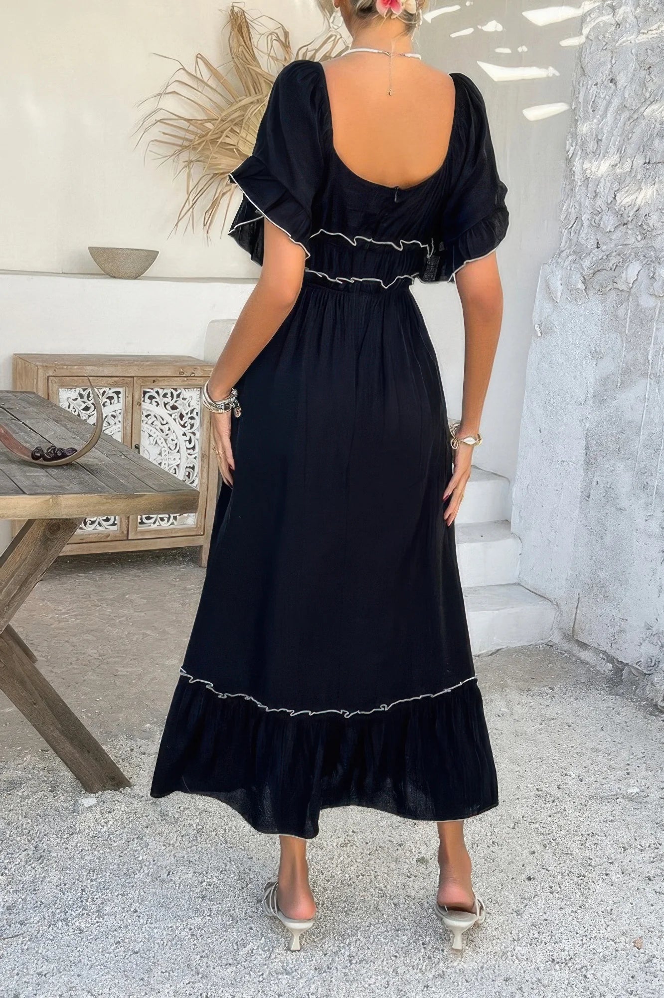 Woman wearing a black dress with ruffled details in an outdoor setting.