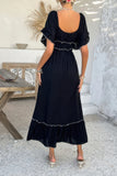 Woman wearing a black dress with ruffled details in an outdoor setting.