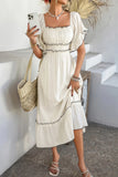 Woman in a white dress holding a phone, standing against a white wall.