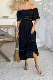 Woman wearing a black off-shoulder dress holding a straw bag in an outdoor setting.