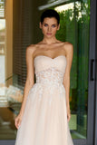 Woman wearing a strapless, beaded gown in an indoor setting with greenery outside.
