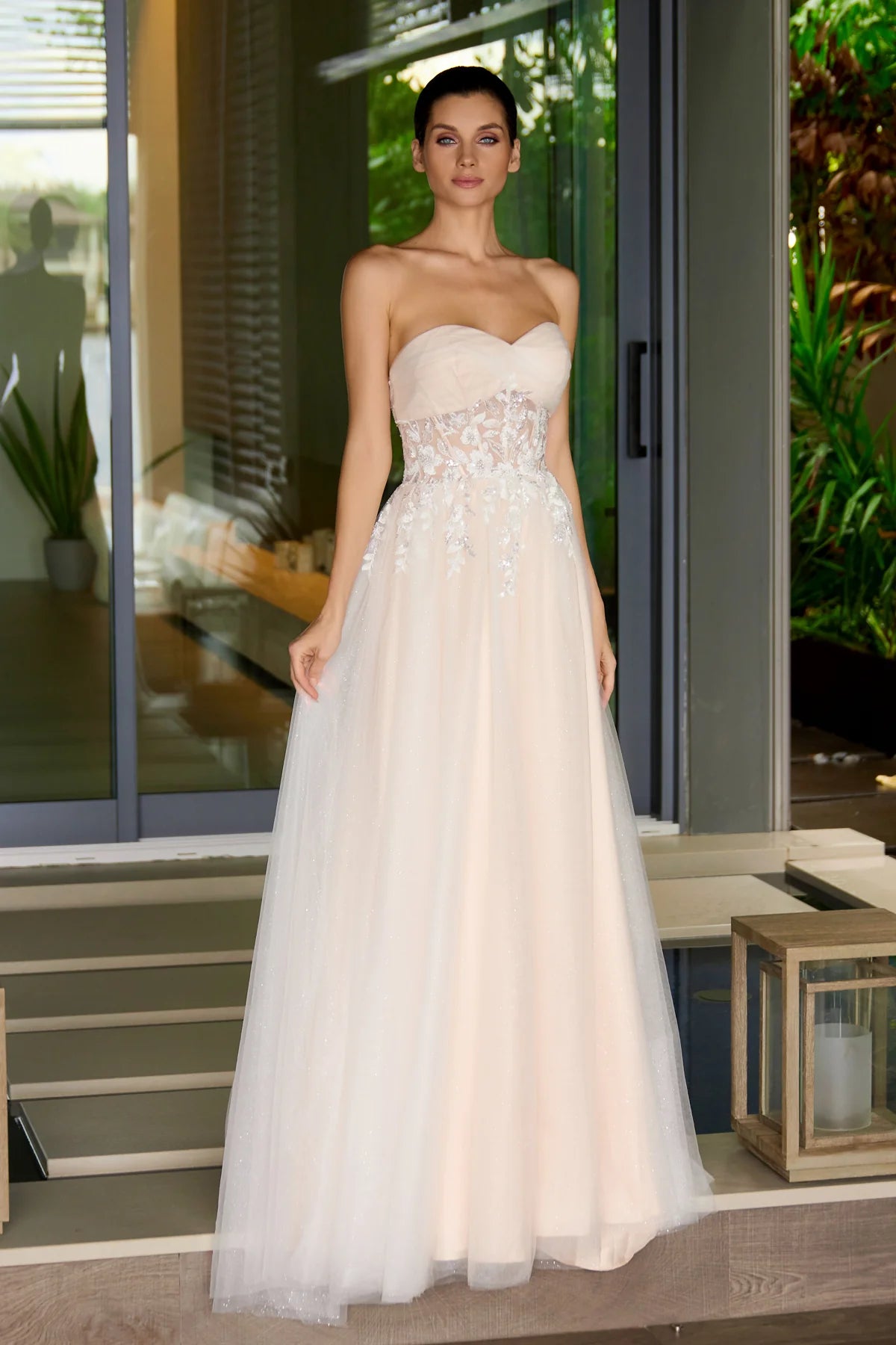 Woman wearing a strapless nude wedding gown with floral details in an outdoor setting.