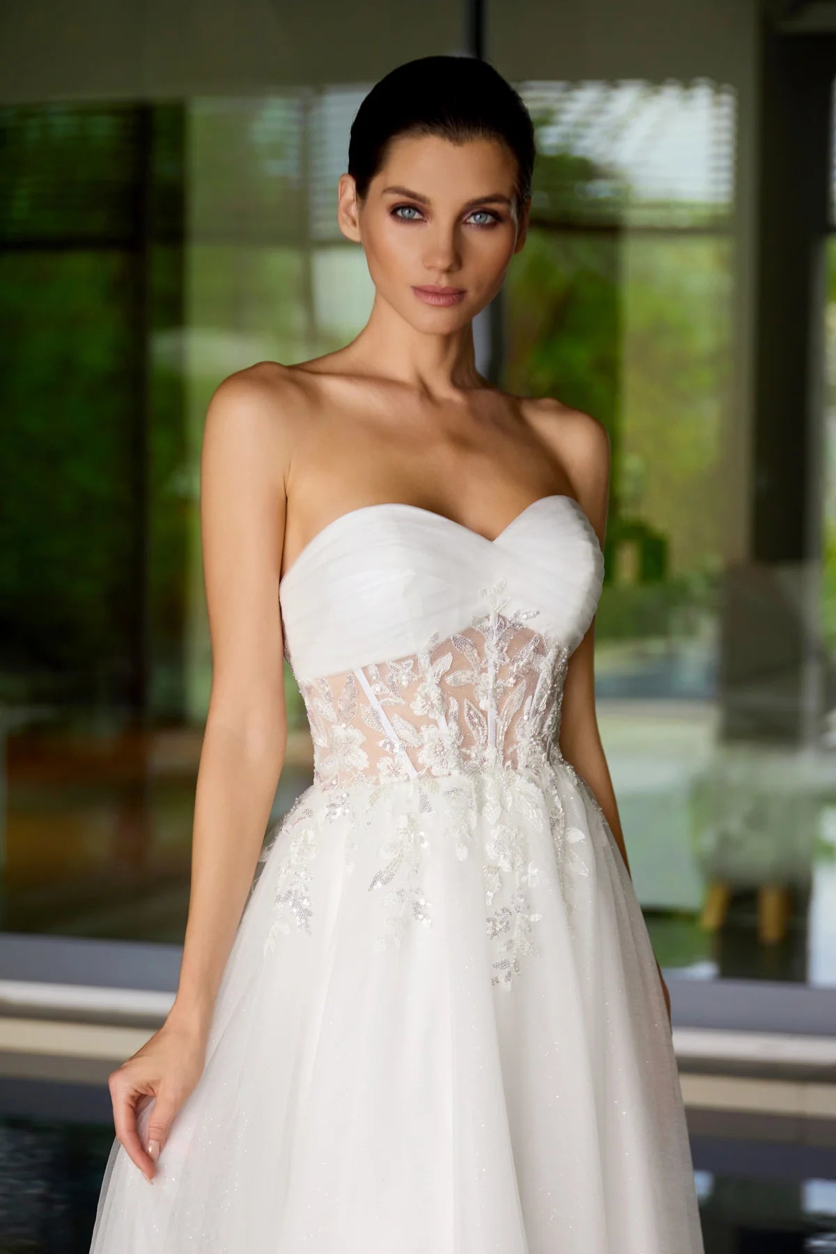 Woman wearing a strapless white wedding dress with lace details in an outdoor setting.