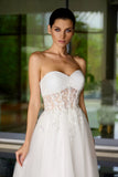 Woman wearing a strapless white wedding dress with lace details in an outdoor setting.