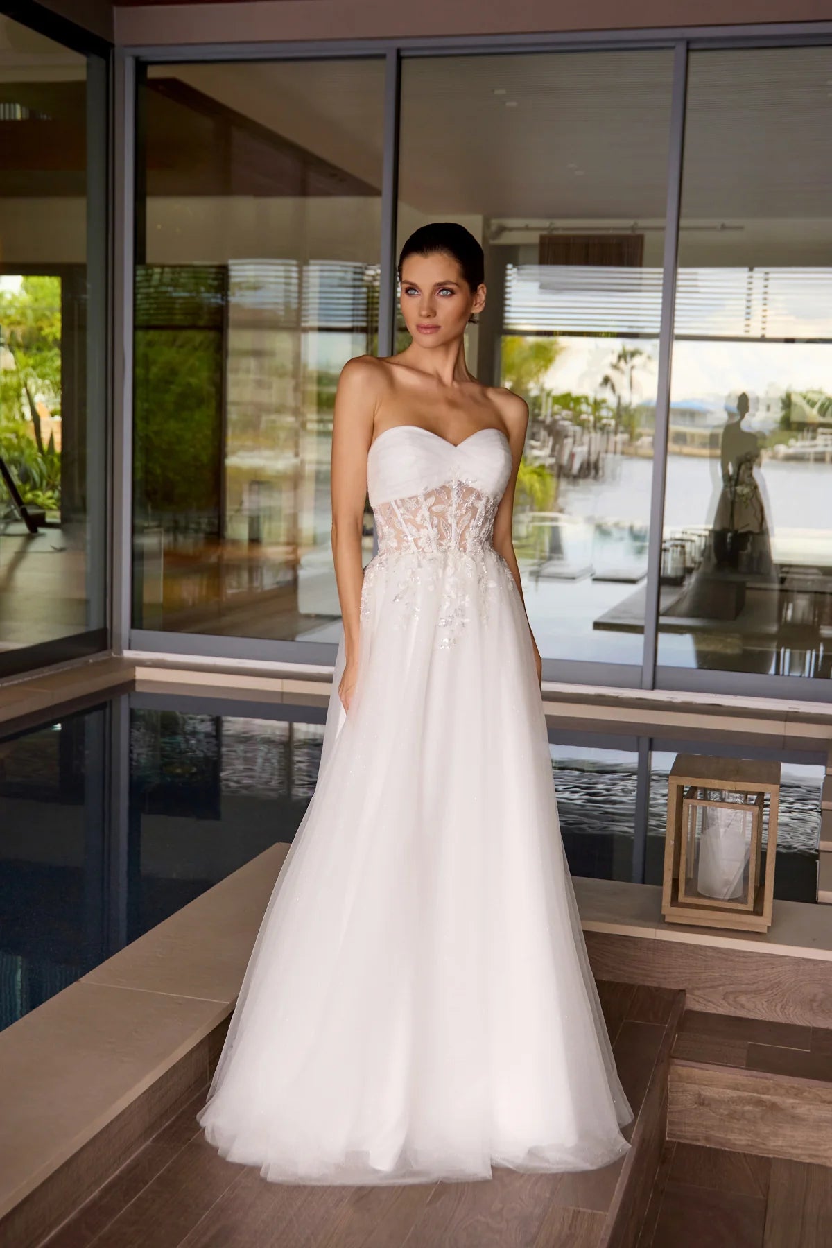 Woman in a white wedding dress standing in front of a modern house with a pool.
