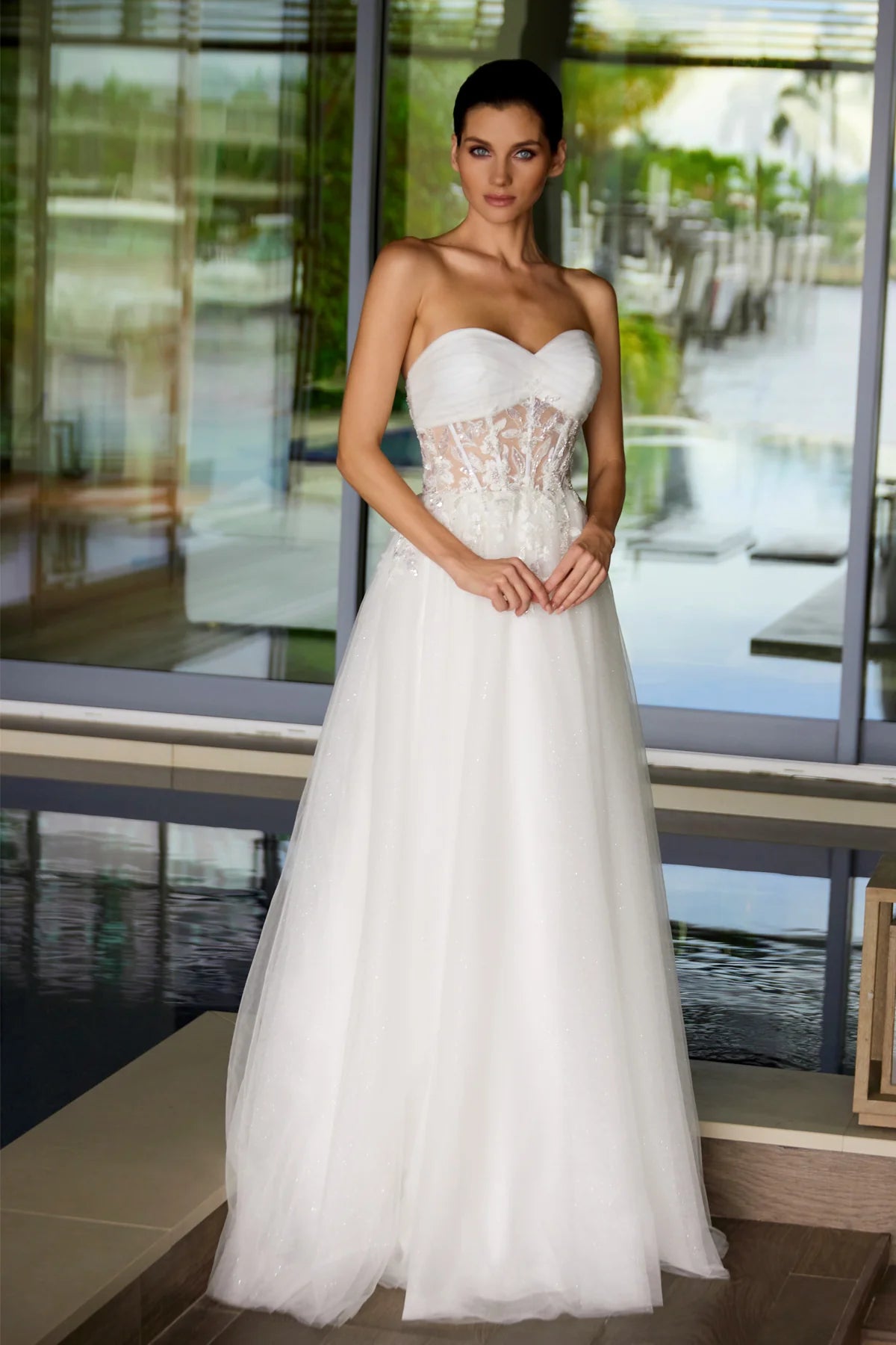 Woman wearing a white strapless wedding dress with intricate detailing in an outdoor setting.