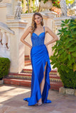 A woman stands outdoors wearing the Juliet JT2697A, a vibrant blue long prom dress with a beaded corset bodice, spaghetti straps, satin skirt with thigh-high slit, paired with strappy high heels.