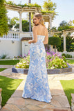 A woman stands outdoors on a stone path in the Long Prom Dress: Juliet JT2737A, featuring a strapless corset bodice and blue and white florals cascading down the floor-length gown, with a garden and pergola in the background.