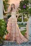 At sunset, a woman stands outdoors in the Juliet JT2739S long prom dress, featuring a strapless floral corset bodice and flowing tiered chiffon A-line skirt. She rests her hand on a column and gazes to the side.