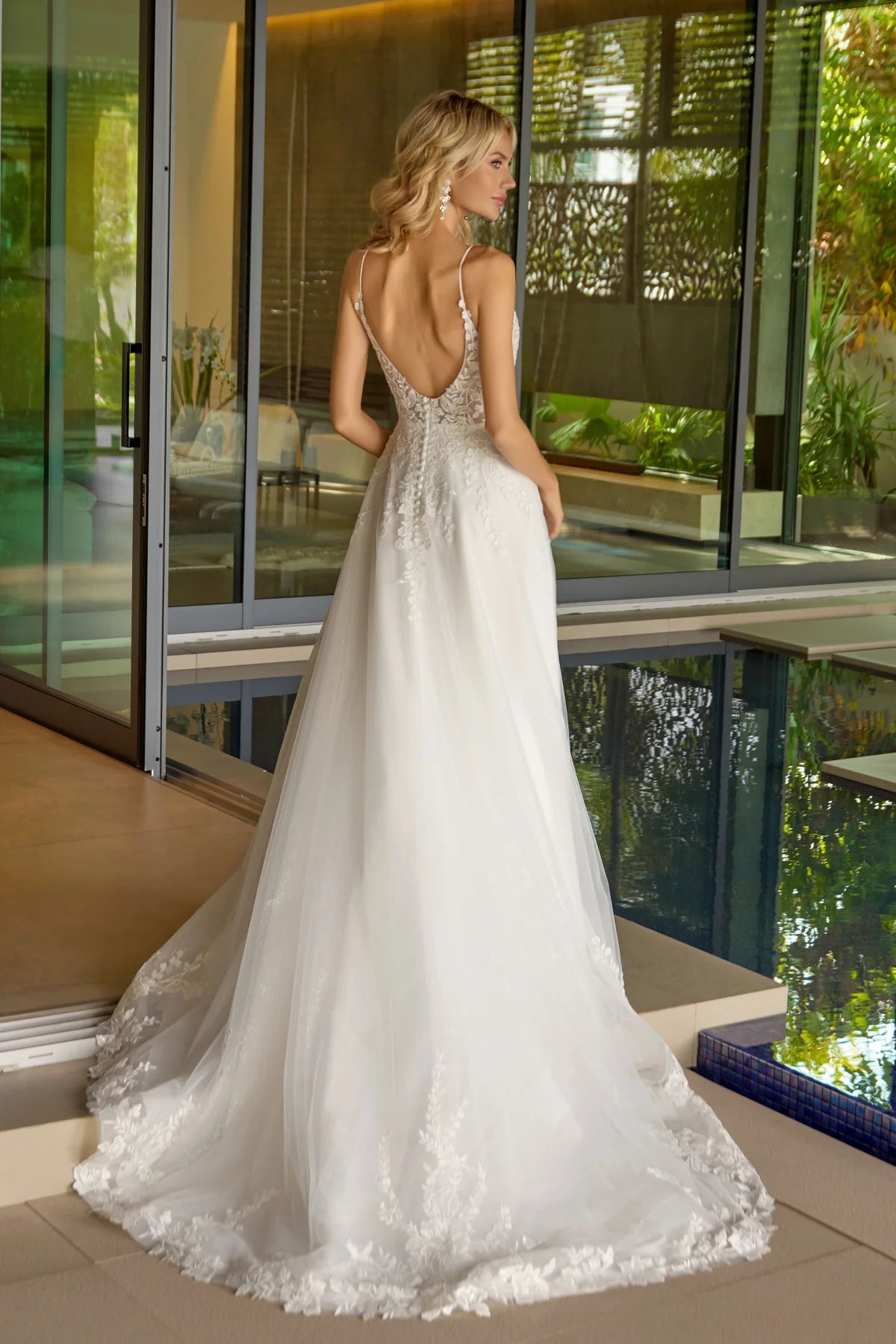 Woman in a white wedding dress with an open back standing by a poolside.