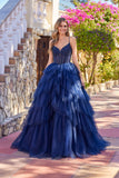 A woman stands outdoors in sunlight by a stone staircase and blooming bougainvillea, wearing the Long Prom Dress: Juliet JT2611N—a navy blue gown with a layered tulle skirt and fitted bodice.