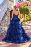 A woman stands outdoors before stone stairs, wearing the Juliet JT2611N long prom dress—a navy blue glitter tulle ball gown with a corset-style back and tiered skirt.