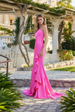 Wearing the Juliet JT2727H Long Prom Dress, a woman stands outdoors on a stone path near a white villa, surrounded by greenery and vines for a charming backdrop.