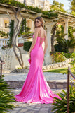A woman stands outdoors on a stone path in front of a villa, wearing the fitted, bright pink Long Prom Dress: Juliet JT2727H with a lace-up back detail—creating a stunning prom look amidst lush greenery.