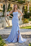A woman stands outdoors on stone pavement wearing the Juliet JT2727H Long Prom Dress in periwinkle, featuring spaghetti straps, a fitted bodice, and ruffle detailing on the floor-length skirt.