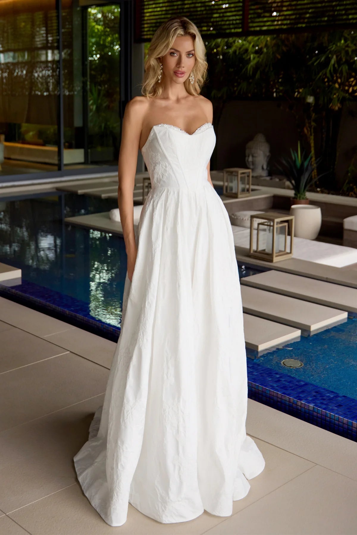 Woman in a strapless white wedding dress standing by a poolside.