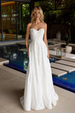 Woman in a white strapless gown standing by a poolside.