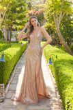 A woman stands on a stone garden path, surrounded by greenery and sunlight, wearing the Juliet JT2730H Long Prom Dress with thin straps, sparkling sequins, and a high leg slit.