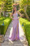 Wearing the Juliet JT2730H long lilac prom dress with sparkly sequins and a thigh-high slit, a woman stands on a garden stone path, smiling at the camera.
