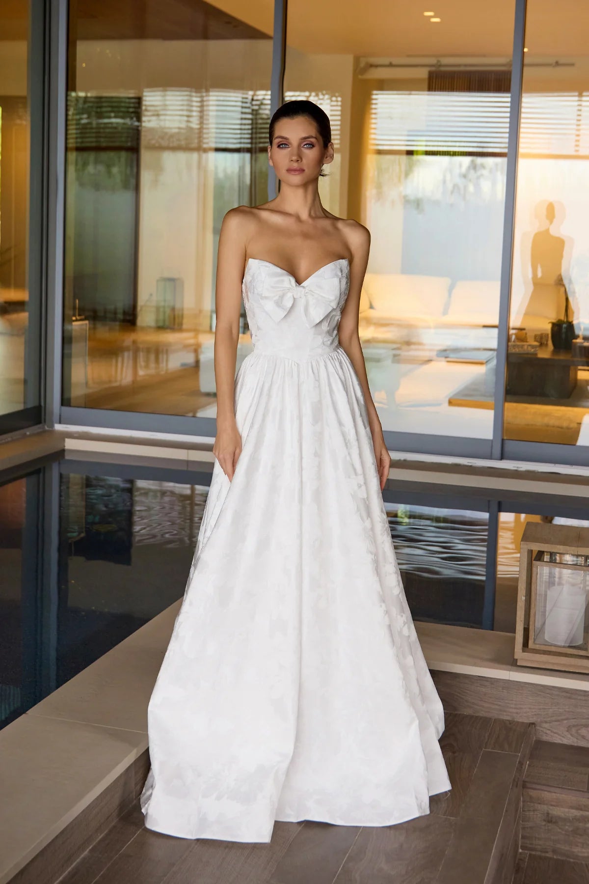 Woman in a white strapless dress standing in a modern indoor setting.