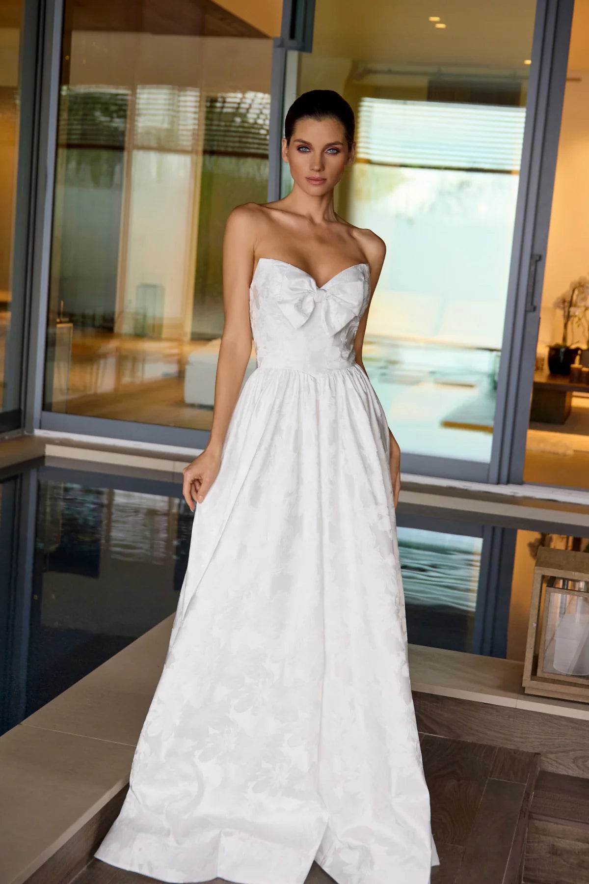 Woman wearing a white strapless dress with a bow detail in an indoor setting.