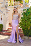 A woman wears the Juliet JT2729H long prom dress, featuring a strapless beaded bodice and thigh-high slit, while standing outdoors on tiled steps near green plants and stone owl statues.