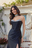 A woman stands outdoors in front of a building, smiling at the camera while wearing the Long Prom Dress: Juliet JT2698A—a strapless satin gown with silver hot stone embellishments and a matching choker.