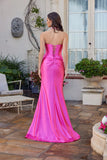 A woman stands outdoors, surrounded by plants and patio furniture, wearing the elegant Juliet JT2698A long prom dress—a pink strapless satin gown with a fitted corset bodice and flared skirt that shines beautifully.