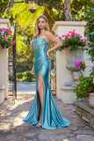 A woman in the Juliet JT2708K Long Prom Dress in sea green—shiny satin, strapless with a high slit and wrap sheath skirt—stands outdoors on a stone path among greenery and potted flowers.