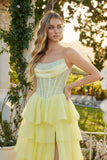 A woman wears the Juliet JT2738S long prom dress, featuring a strapless beaded corset bodice and pastel yellow chiffon ruffle skirt, as she stands outdoors by greenery and flowers, gazing to the side.