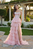A woman stands outdoors in the Juliet JT2738S long prom dress, featuring a strapless corset bodice and tiered chiffon ruffle skirt with a high slit, surrounded by greenery and stone columns.
