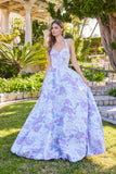 A woman stands outdoors looking over her shoulder, wearing the Juliet JT2742A long prom dress—a strapless, floor-length gown with floral texture and a light blue and lavender pattern.