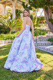 A woman stands outdoors looking over her shoulder, wearing the Juliet JT2742A long prom dress—a strapless, floor-length gown with floral texture and a light blue and lavender pattern.