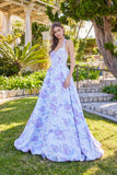 A woman stands outdoors on grass wearing the Juliet JT2742A Long Prom Dress in Lavender Amethyst, featuring a floral-textured design, corset bodice, and halter neckline; trees and a stone path are in the background.