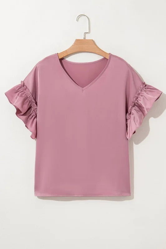 Pink blouse with ruffled sleeves on a wooden hanger against a white background