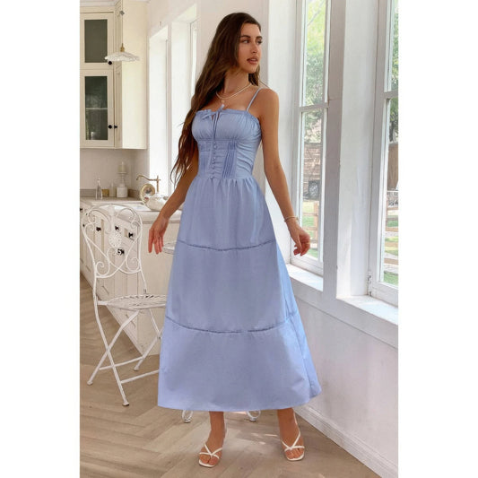 Woman in a light blue dress standing in a bright room with large windows.